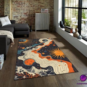 May include: A rectangular area rug with a celestial design. The rug features a dark blue background with orange, yellow, and cream-colored celestial bodies and flowing lines. The rug is placed on a wooden floor in a living room setting.