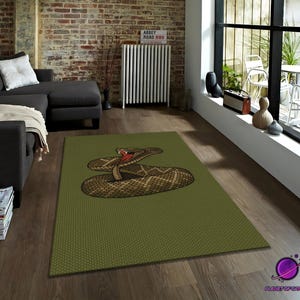 Può includere: Un tappeto rettangolare verde con un'illustrazione dettagliata di un serpente a sonagli arrotolato con la bocca aperta, che rivela una lingua rossa. Il serpente è marrone e beige con un motivo a rombi. Il tappeto ha una superficie strutturata.