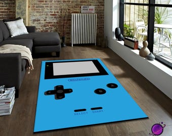 May include: A rectangular, light blue rug with a large graphic of a classic handheld video game console. The rug features black control buttons, a screen, and the Nintendo logo. The rug is on a wooden floor.