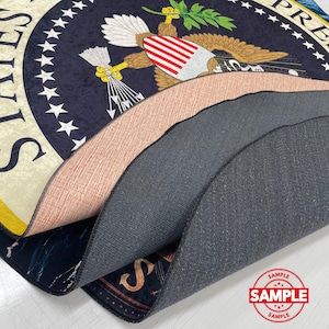 May include: A layered rug with the Presidential Seal design, featuring a navy blue background with white stars and a central eagle emblem. The rug's edges reveal different textures and colours, including a peach and grey layer. A "SAMPLE" stamp is visible.