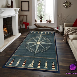 May include: A rectangular blue nautical rug with a compass rose design. The rug has a border with lighthouse illustrations and rope detailing. It is placed on a dark wood floor in a living room setting.