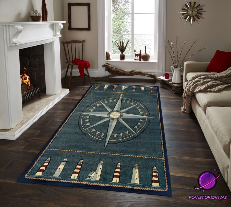 May include: A rectangular blue nautical rug with a compass rose design. The rug has a border with lighthouse illustrations and rope detailing. It is placed on a dark wood floor in a living room setting.