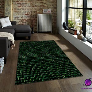 Puede incluir: Una alfombra rectangular negra con un patrón de código binario verde. La alfombra está colocada sobre un suelo de madera en un salón, cerca de un sofá gris oscuro y una ventana. El diseño de la alfombra presenta un patrón repetido de ceros y unos verdes.