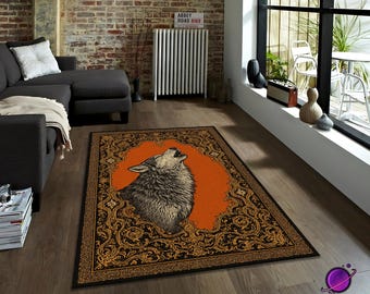 May include: A rectangular area rug featuring a howling wolf illustration. The wolf is depicted in shades of gray and black against an orange background, framed by an ornate black and gold border. The rug is placed on a wooden floor.