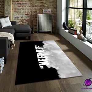 Può includere: Un tappeto rettangolare bianco e nero con la scritta "KEEP OFF" in bianco. Il tappeto ha uno sfondo nero sul lato sinistro e un design a nuvola sul lato destro. È posizionato su un pavimento in legno.