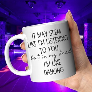 May include: White ceramic coffee mug with black text that reads "It may seem like I'm listening to you but in my head I'm line dancing."