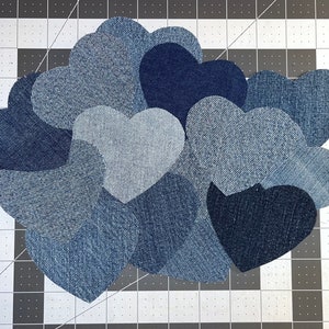 May include: A collection of denim heart shapes in various shades of blue, arranged in a cluster. The hearts are sewn together to create a decorative piece.