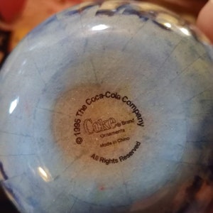 K&ouml;nnte beinhalten: Ein blauer und wei&szlig;er Glas-Anh&auml;nger mit dem Logo der Coca-Cola Company und dem Text "&copy; 1995 The Coca-Cola Company Coke&reg; Brand Ornaments Made in China All Rights Reserved".