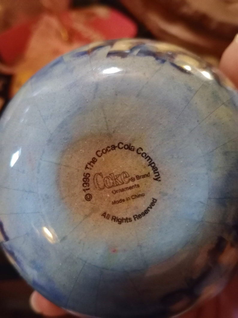 K&ouml;nnte beinhalten: Ein blauer und wei&szlig;er Glas-Anh&auml;nger mit dem Logo der Coca-Cola Company und dem Text "&copy; 1995 The Coca-Cola Company Coke&reg; Brand Ornaments Made in China All Rights Reserved".