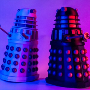 May include: Two Dalek figurines, one black and one white, with red accents. The Daleks are from the Doctor Who television series.