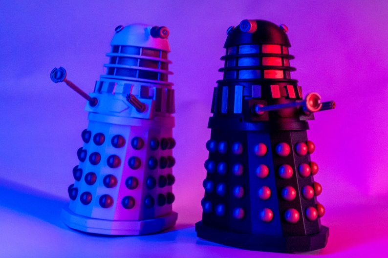 May include: Two Dalek figurines, one black and one white, with red accents. The Daleks are from the Doctor Who television series.
