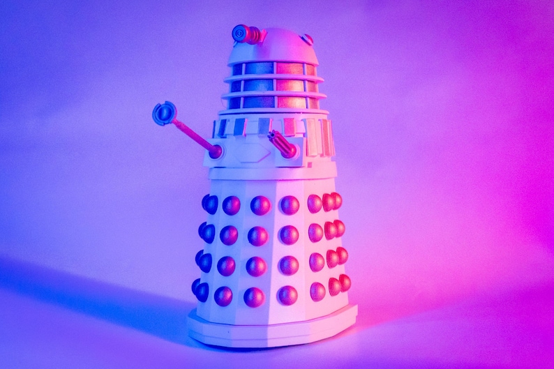 May include: A white robot with a dome-shaped head and a large, round body. The robot has a single, long, thin arm with a weapon at the end. The robot is standing on a purple and blue background.