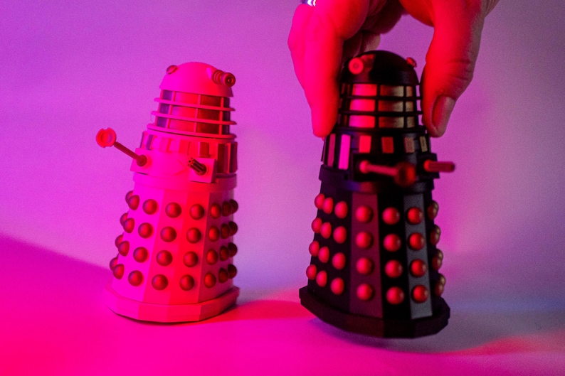 May include: Two toy Daleks, one black and one white, with red accents. The Daleks are from the Doctor Who television series.