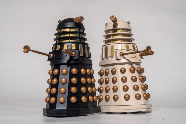 May include: Two Dalek figurines, one black and one white, with gold accents. Both Daleks have a raised dome with a single eye and a gun arm.