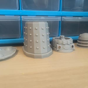 May include: Four gray 3D printed pieces of a Dalek model, including the base, dome, and two sections of the body.