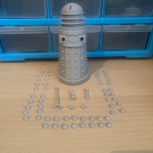 May include: A gray plastic model kit of a Dalek, a fictional robot from the British science fiction television series Doctor Who. The kit includes the main body of the Dalek, three guns, and a number of small dome-shaped pieces.