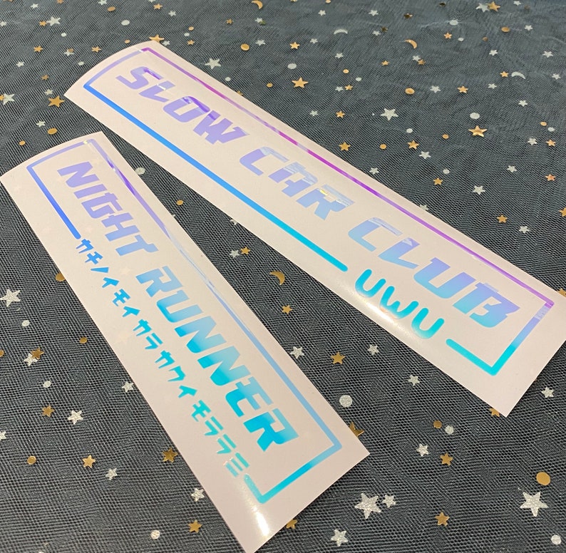 May include: Two rectangular adhesive decals with a holographic finish. One decal features the text SLOW CAR CLUB UWU in a bold font. The second decal displays the text NIGHT RUNNER with Japanese characters below, both enclosed in a thin rectangular border.
