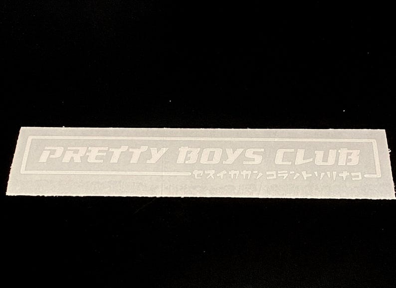 May include: A rectangular white sticker featuring the text PRETTY BOYS CLUB in a bold, stylised font enclosed within a thin white border. Below the main text, there is a line of Japanese katakana characters also enclosed in the border.