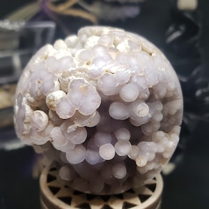 May include: A purple and white agate sphere with a textured surface. The sphere is sitting on a wooden stand.