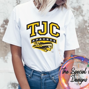 May include: White t-shirt with a yellow and black graphic of the letters "TJC" above the word "Apaches" and a Native American headdress design. The Special Gift Designs logo is visible in the lower right corner.