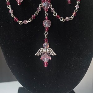 May include: A silver angel charm pendant with pink crystal beads and a silver chain.