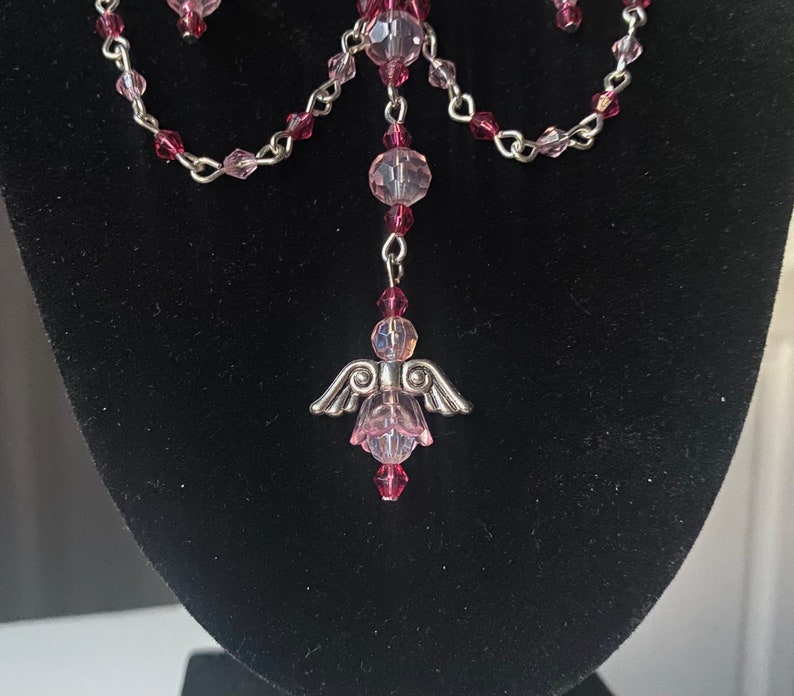 May include: A silver angel charm pendant with pink crystal beads and a silver chain.