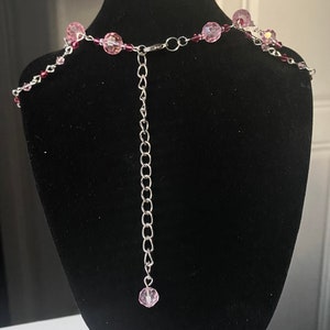 May include: A silver chain necklace with pink glass beads. The necklace has an adjustable length.