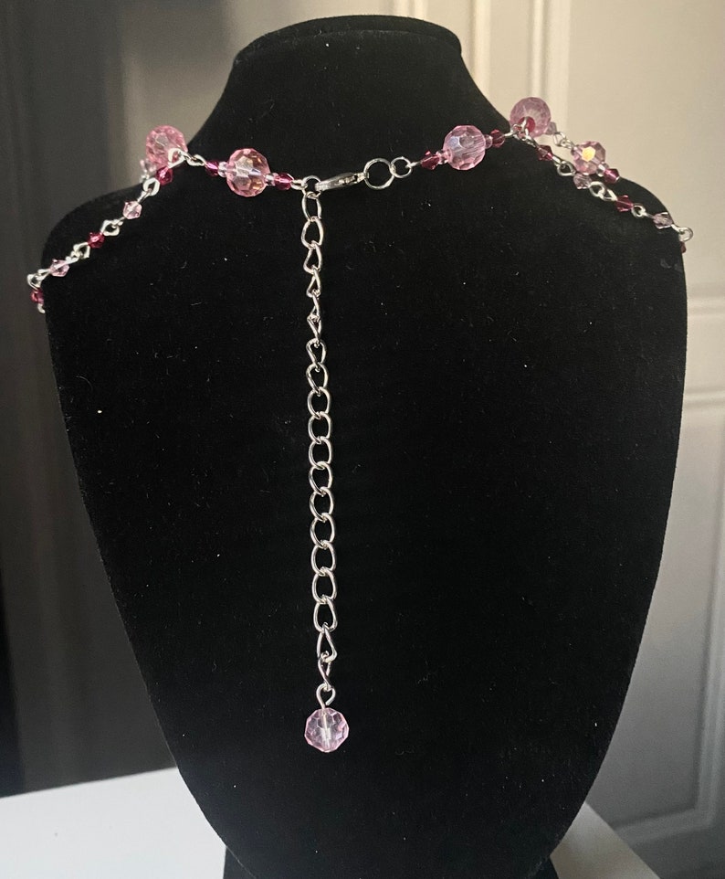 May include: A silver chain necklace with pink glass beads. The necklace has an adjustable length.
