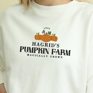 May include: White long-sleeve sweatshirt with a graphic of pumpkins and the text "Hagrid's Pumpkin Farm Magically Grown" and the year "1991" above the graphic.