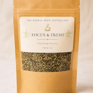 May include: A brown kraft paper pouch containing loose leaf tea, with a clear window showing the green and yellow herbal blend. The label reads THE HERBAL BREW APOTHECARY, FOCUS & FRESH, Clean Energy Focus Tea, and Net wt. 1 oz, with leaf illustrations.