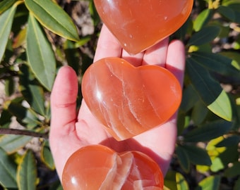 May include: Three orange calcite heart shaped crystals. The crystals are polished and have white veins running through them.