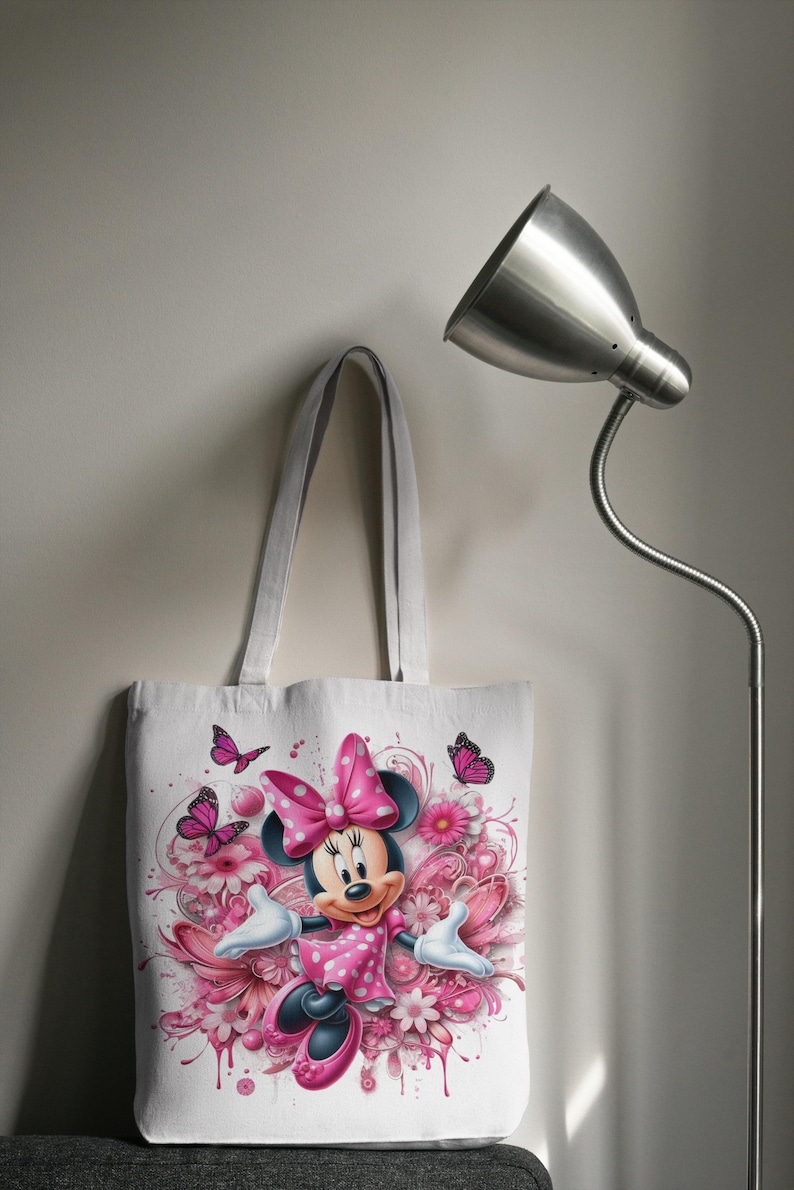 May include: White canvas tote bag with a pink and white Minnie Mouse design. Minnie Mouse is wearing a pink polka dot dress and a pink bow. The design includes pink flowers and butterflies.