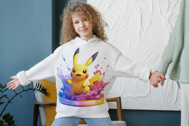 May include: White hoodie with a colorful graphic of Pikachu, a yellow electric-type Pokemon, surrounded by blue, purple, and pink paint splatters.