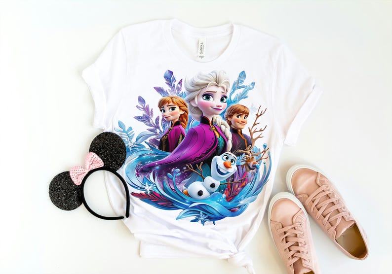 Pu&ograve; includere: Maglietta bianca con una stampa grafica colorata di Elsa, Anna e Olaf del film Frozen. I personaggi sono circondati da vortici blu e viola.