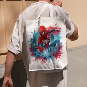 May include: A white tote bag with a colorful graphic of Spider-Man swinging through the city skyline. The graphic features red, blue, and white colors with a splash of paint effect.