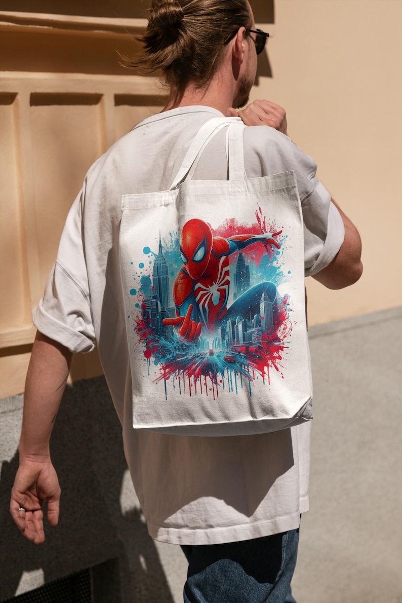 May include: A white tote bag with a colorful graphic of Spider-Man swinging through the city skyline. The graphic features red, blue, and white colors with a splash of paint effect.