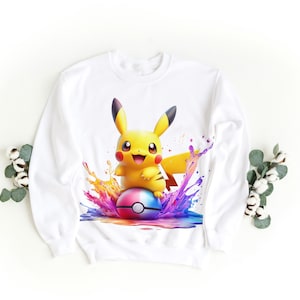 May include: White sweatshirt with a colorful graphic of Pikachu, a popular Pokemon character, holding a Pokeball. The graphic features a splash of colorful paint.