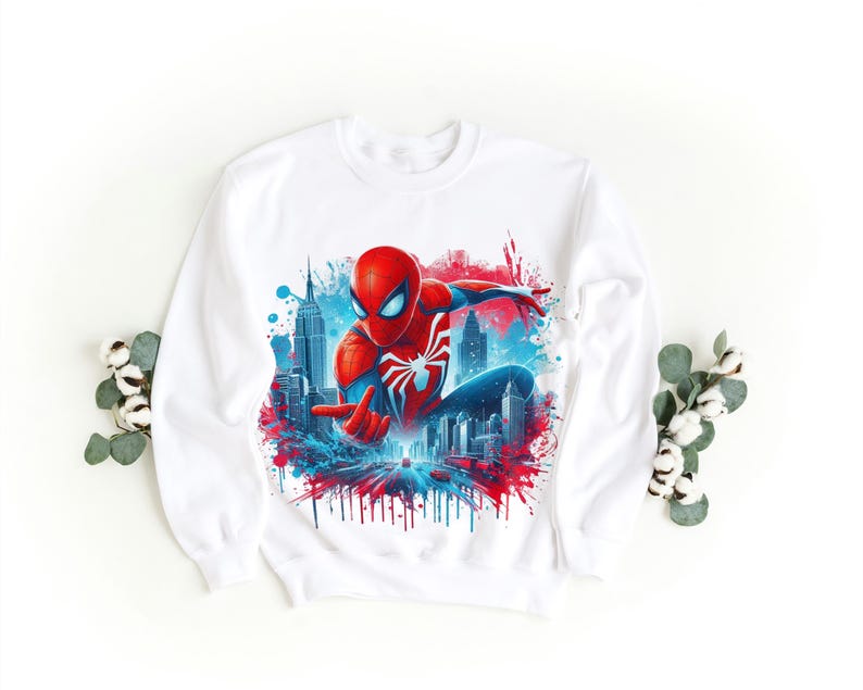 May include: White sweatshirt with a red and blue graphic print of Spiderman swinging through a cityscape. The graphic has a paint splatter effect.