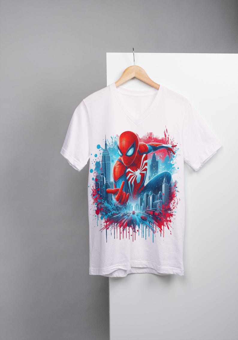 May include: White t-shirt with a colorful graphic print of Spider-Man in a superhero pose, with a cityscape background and red and blue paint splatters.