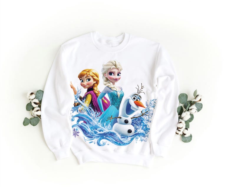 Pu&ograve; includere: Felpa bianca con una stampa colorata di Elsa, Anna e Olaf del film Frozen. I personaggi sono circondati da onde d'acqua blu.