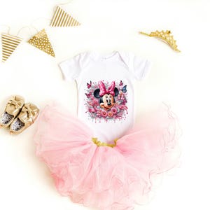 May include: A white bodysuit with a pink and black Minnie Mouse graphic, a pink tulle tutu, and gold shoes. The bodysuit has a watercolor-style design with flowers and butterflies.