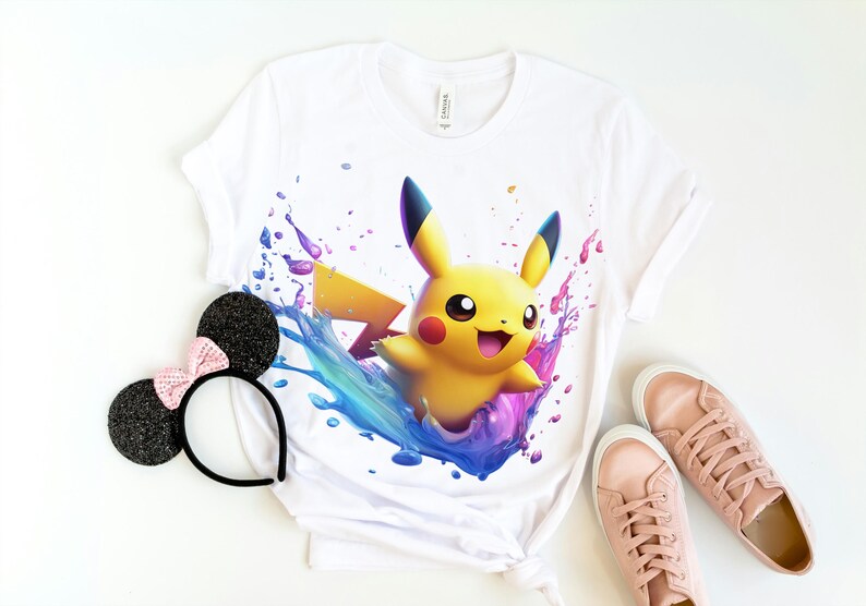 May include: White t-shirt with a colorful graphic of Pikachu, a yellow electric-type Pokemon, emerging from a splash of paint.