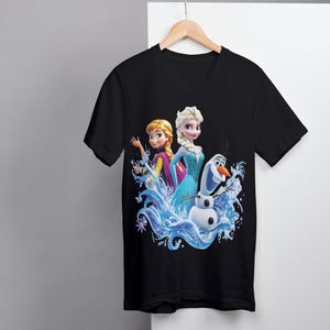 Pu&ograve; includere: Maglietta nera a collo a V con una stampa grafica colorata di Elsa e Anna di Frozen, in piedi in un'onda d'acqua con Olaf il pupazzo di neve.