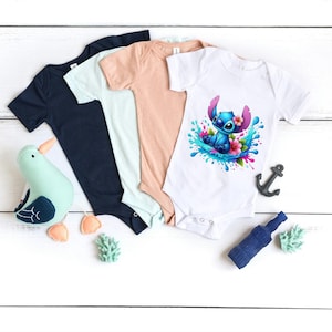 May include: Three baby onesies in different colors: navy blue, light blue, and peach. The white onesie has a colorful graphic of Stitch from Lilo & Stitch surfing on a wave with flowers.