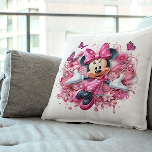 May include: A white pillow with a pink and white floral design featuring Minnie Mouse in a pink polka dot dress.  She is surrounded by pink flowers and butterflies.