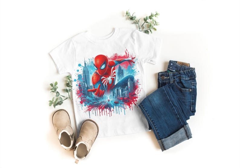 May include: White t-shirt with a colorful graphic of Spiderman swinging through the city. The graphic has red, blue, and white paint splatters.