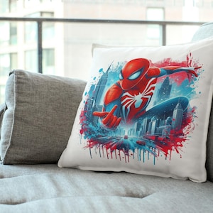 May include: A white pillow with a colorful graphic of Spider-Man swinging through a city skyline. The graphic features a red and blue Spider-Man suit with a white spider logo. The background is a blue and red watercolor effect.