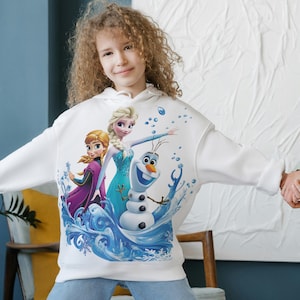 Pu&ograve; includere: Felpa con cappuccio bianca con una stampa grafica colorata dei personaggi Elsa, Anna e Olaf del film Frozen. I personaggi sono raffigurati in una scena invernale con fiocchi di neve e ghiaccio.