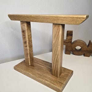 May include: A wooden stand with two upright posts and a horizontal top piece. The stand has a rectangular base.