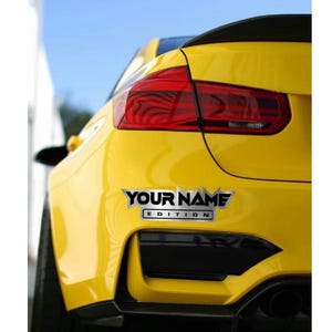 Puede incluir: Un coche amarillo con un aler&oacute;n negro y una calcoman&iacute;a plateada que dice "YOUR NAME EDITION".